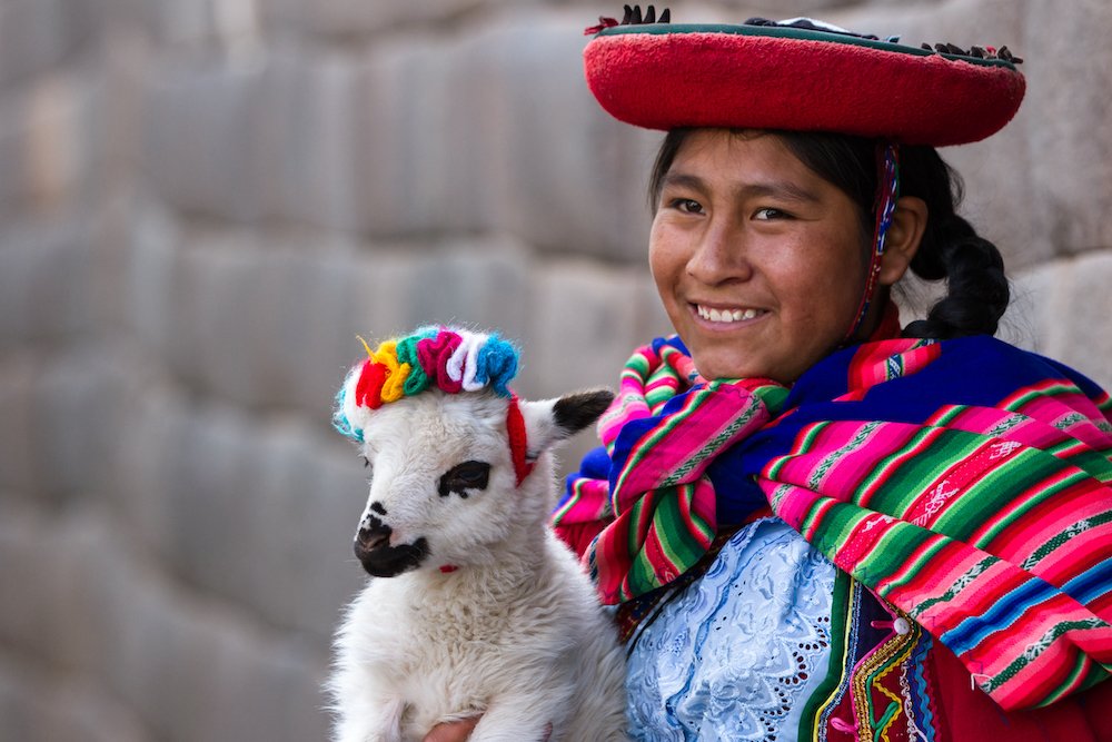 Cusco, Peru - May 14 : Jenni, a young woman dressed in colorful traditional native Peruvian closing holding a baby Lamb with Inca walls in the background. May 14 2016, Cusco Peru.